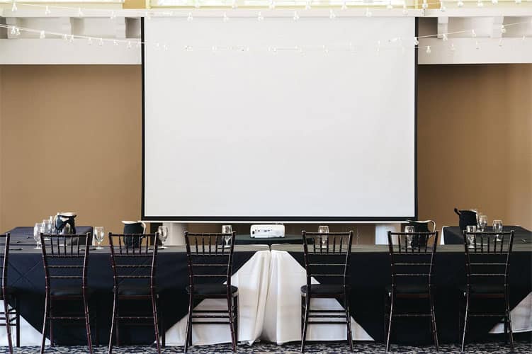 Room with chairs and tables, featuring a large screen for presentations or conferences.