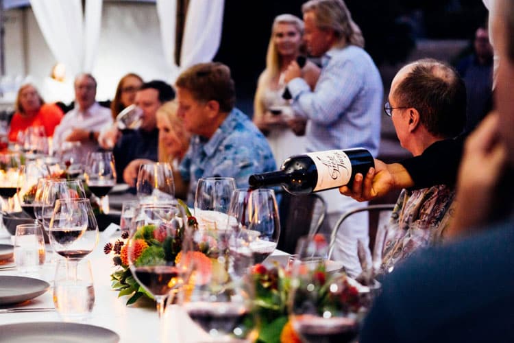 A group of people sitting at a long table with wine glasses, enjoying a social gathering.