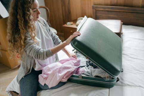 A woman sitting on a bed with an open suitcase beside her.